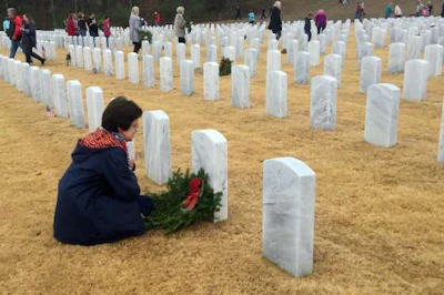 A woman sits besides the grave of her loved one, a veteran, after placing a remembrance wreath on it.