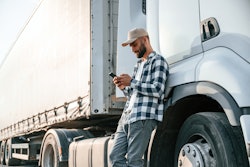 Truck driver leaning against tractor-trailer