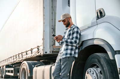 Truck driver leaning against tractor-trailer