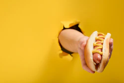 Hand holding hot dog on yellow background