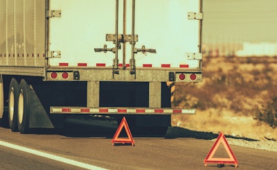Tractor-trailer on the side of the highway with two warning triangles
