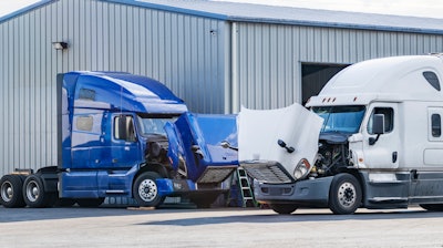 Two trucks with hoods up waiting for repairs