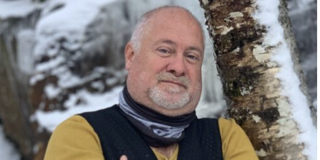 Mature man in winter clothing standing near birch tree with snowy background