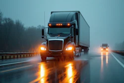 Semi-truck with headlights on during heavy rain and fog on a multi-lane highway
