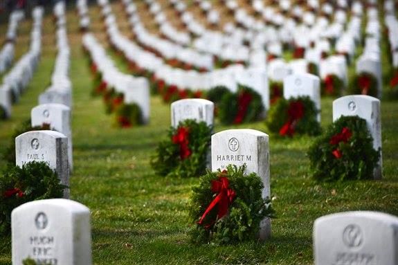 Military cemetery with white headstones in rows decorated with red wreaths and evergreen garland