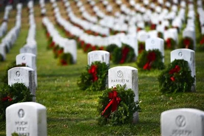 Military cemetery with white headstones in rows decorated with red wreaths and evergreen garland