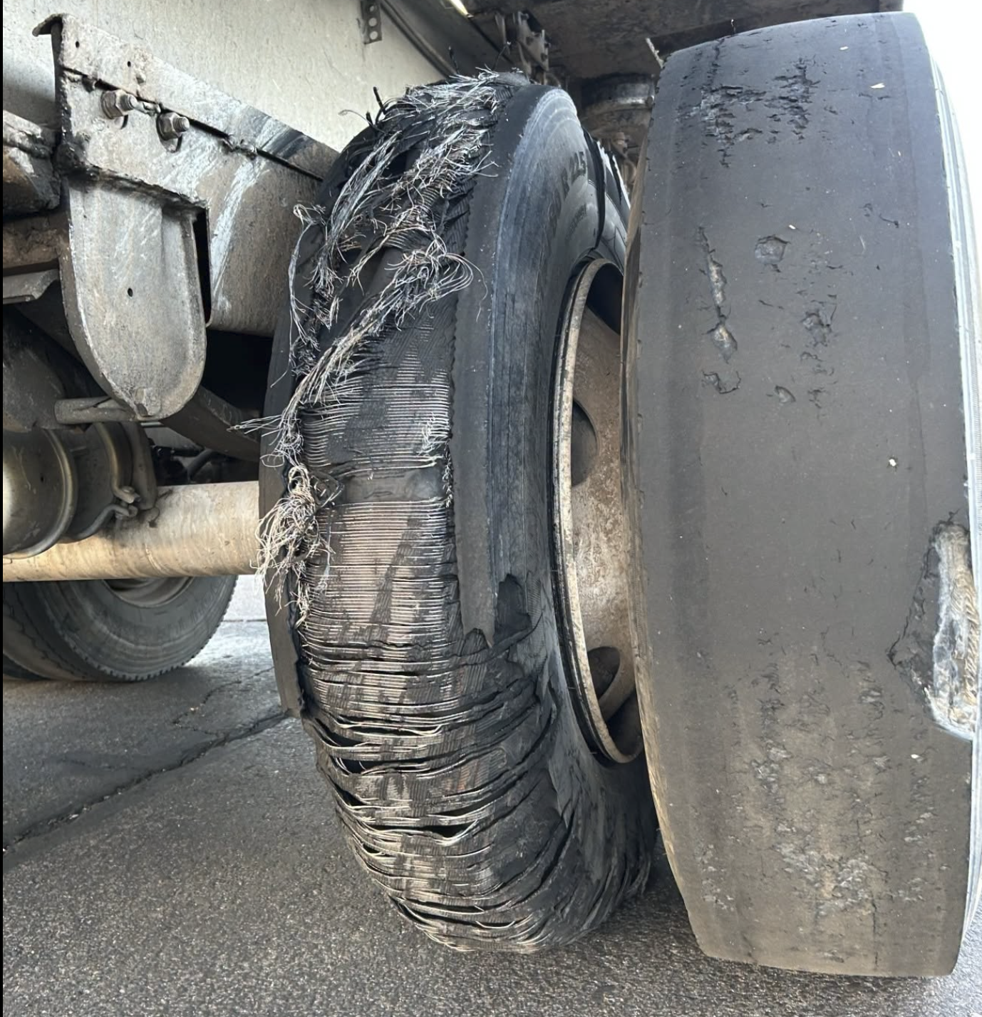 Damaged truck tire with severe tread separation and debris wrapped around the wheel