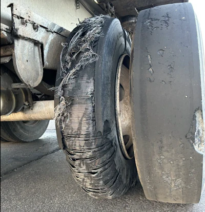 Damaged truck tire with severe tread separation and debris wrapped around the wheel