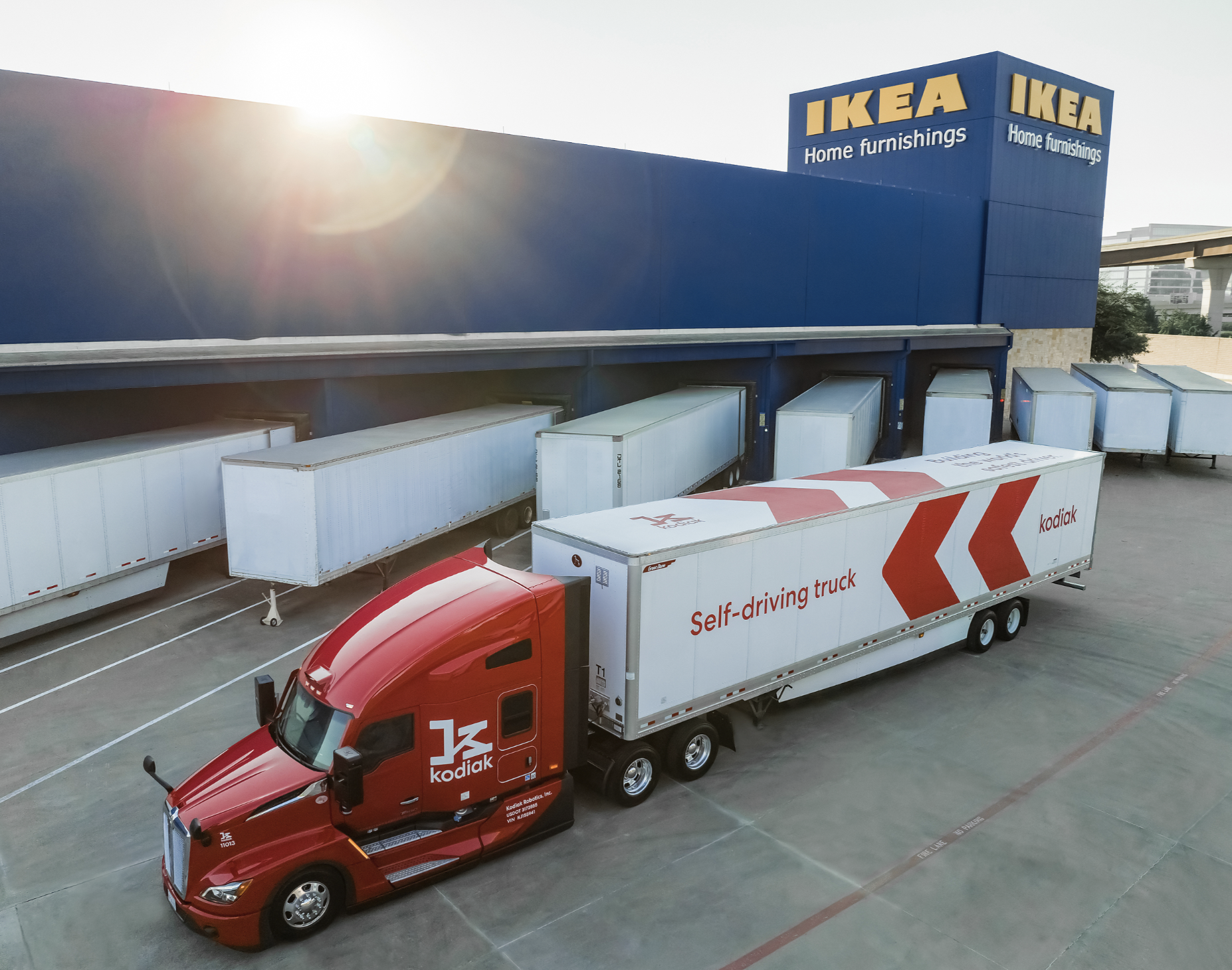 Red Kodiak autonomous delivery truck with white trailer parked at IKEA loading dock with white shipping containers