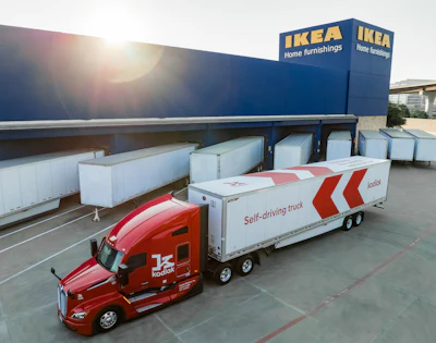 Red Kodiak autonomous delivery truck with white trailer parked at IKEA loading dock with white shipping containers