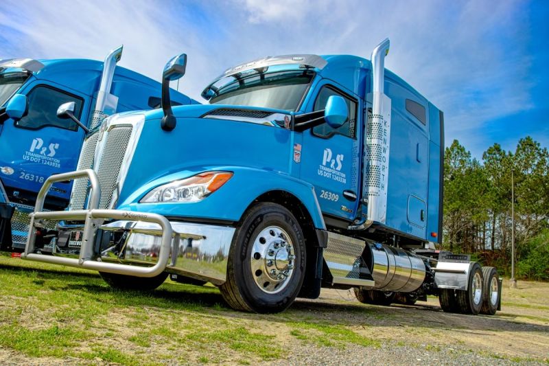 Blue P&S commercial semi-truck with chrome details parked on grass with pine trees in background