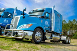 Blue P&S commercial semi-truck with chrome details parked on grass with pine trees in background