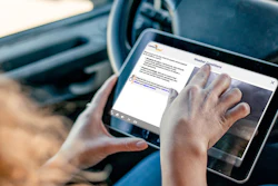 Person holding tablet in car displaying digital interface with steering wheel visible