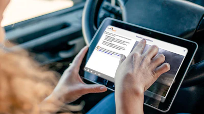 Person holding tablet in car displaying digital interface with steering wheel visible