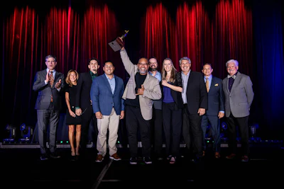 Group of professionals on stage celebrating with an award at a formal event with red curtains