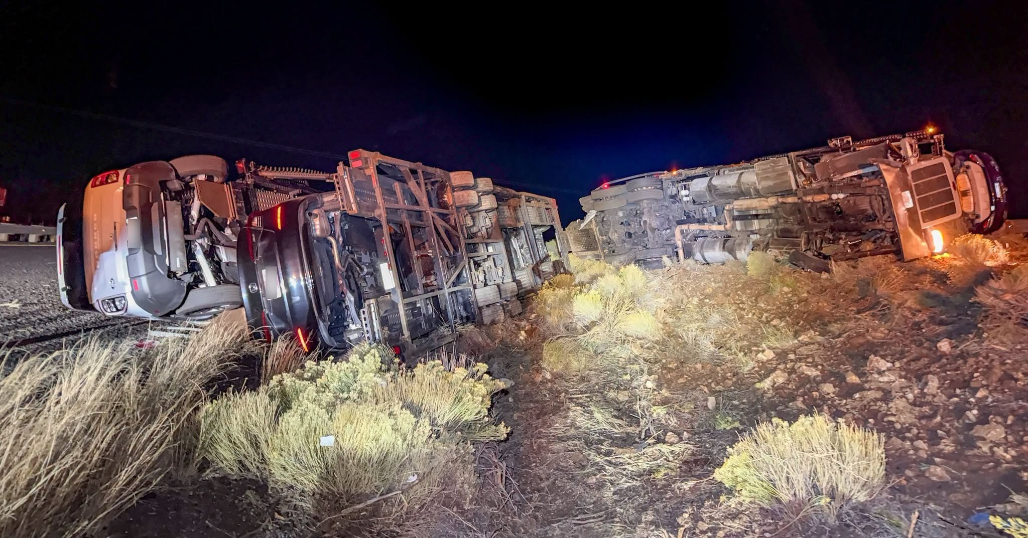 Two overturned vehicles at night on desert terrain with sparse vegetation