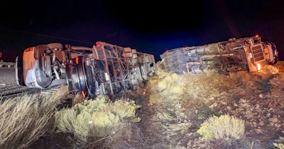 Two overturned vehicles at night on desert terrain with sparse vegetation