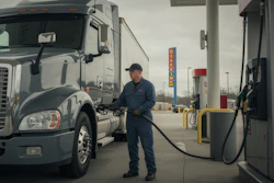 Truck driver refueling a white semi-truck at a commercial fuel station during daytime