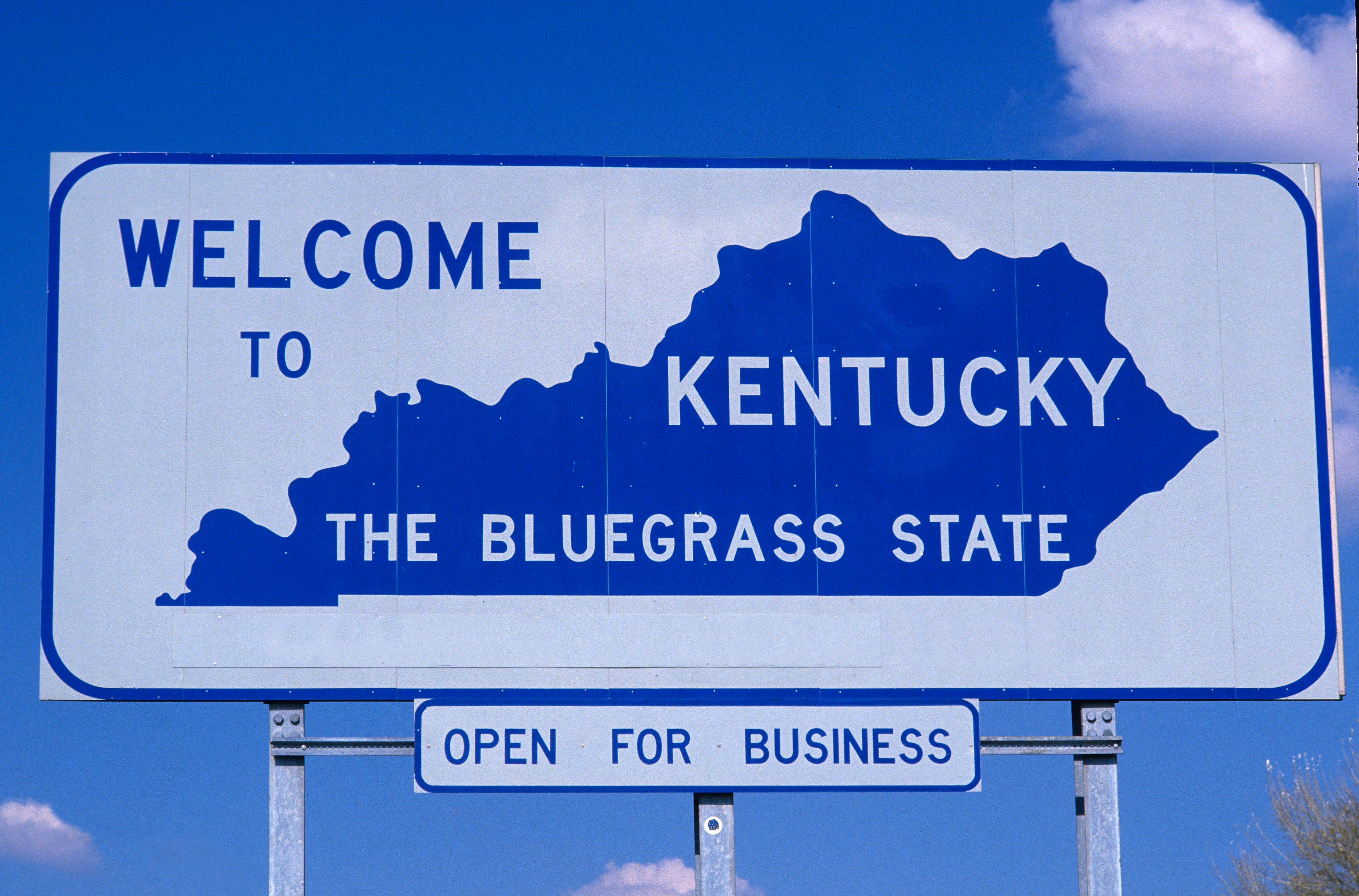Kentucky welcome sign featuring state silhouette with 'The Bluegrass State' slogan and 'Open for Business' banner