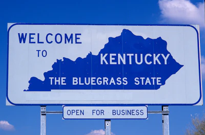 Kentucky welcome sign featuring state silhouette with 'The Bluegrass State' slogan and 'Open for Business' banner