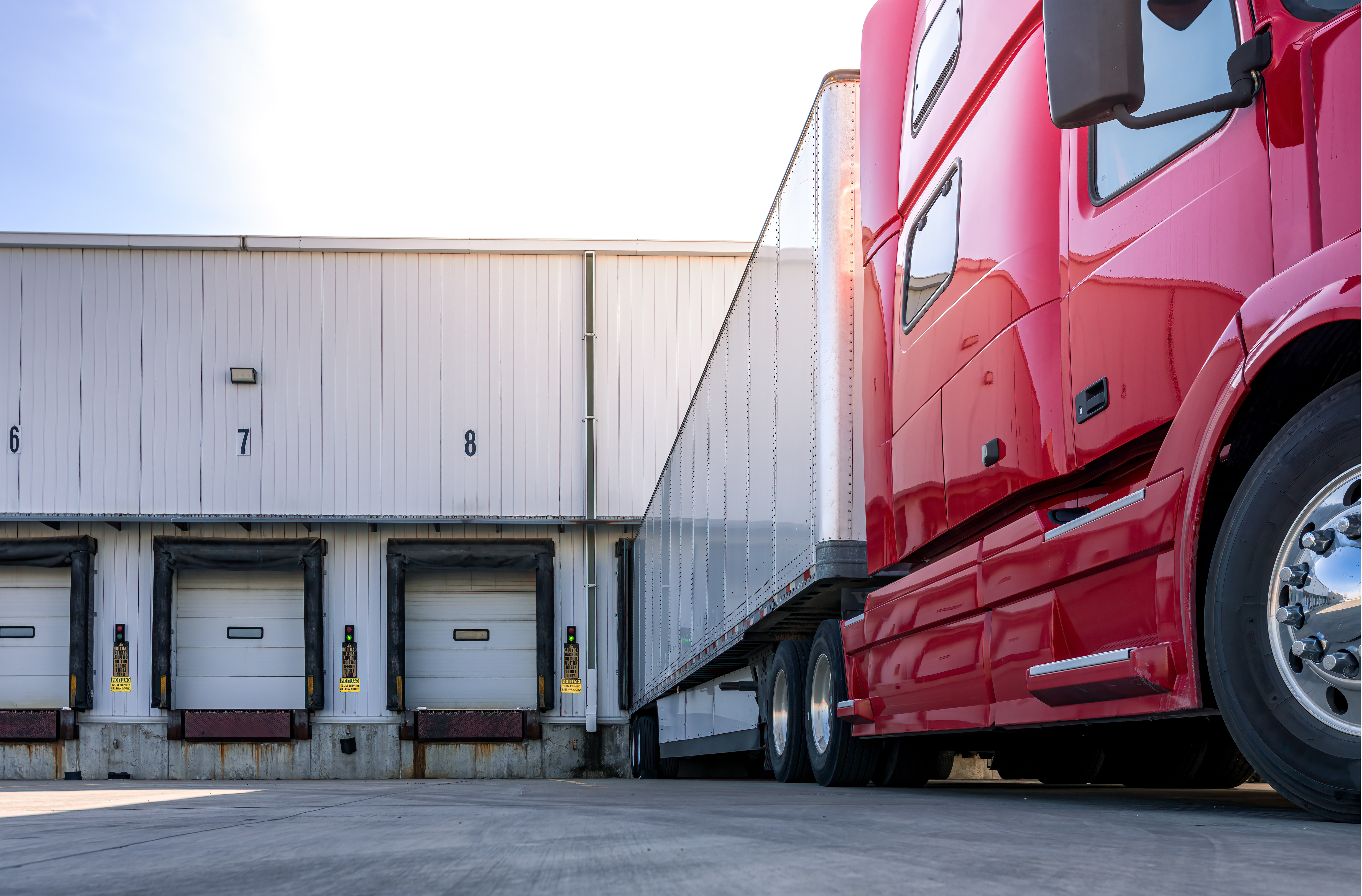 Red semi-truck backed up to white loading dock doors at a warehouse facility