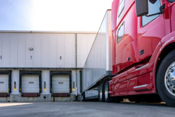 Red semi-truck backed up to white loading dock doors at a warehouse facility