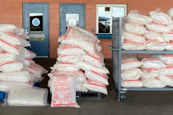 Large quantities of packaged contraband seized by law enforcement stacked against brick wall with institutional doors