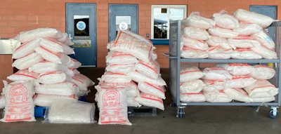 Large quantities of packaged contraband seized by law enforcement stacked against brick wall with institutional doors