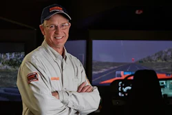 Professional man in work uniform smiling with arms crossed in front of control room simulator display