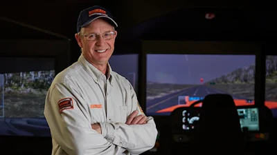 Professional man in work uniform smiling with arms crossed in front of control room simulator display