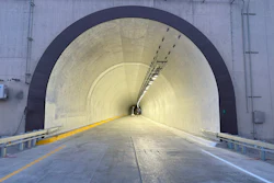 Modern highway tunnel with yellow center line, LED lighting, and metal guardrails extending into distance