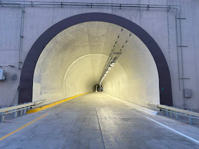 Modern highway tunnel with yellow center line, LED lighting, and metal guardrails extending into distance
