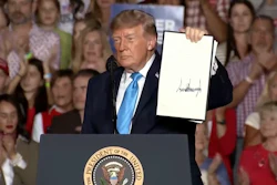 Person at podium holding document during political rally with crowd in background