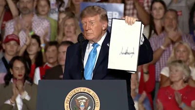 Person at podium holding document during political rally with crowd in background