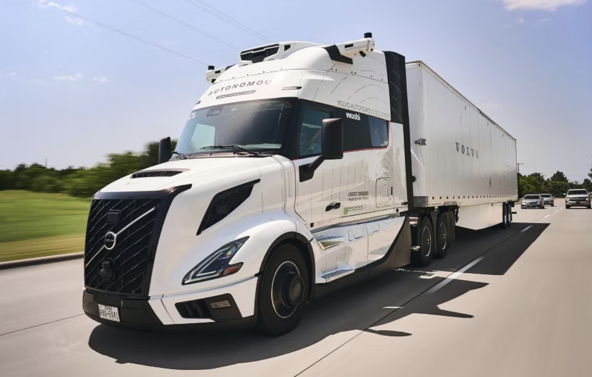White Volvo semi-truck with refrigerated trailer driving on highway with green landscape