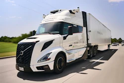 White Volvo semi-truck with refrigerated trailer driving on highway with green landscape