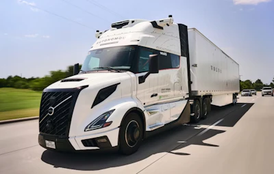 White Volvo semi-truck with refrigerated trailer driving on highway with green landscape