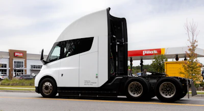 White and black semi-truck with open door at commercial facility with Pilcs signage