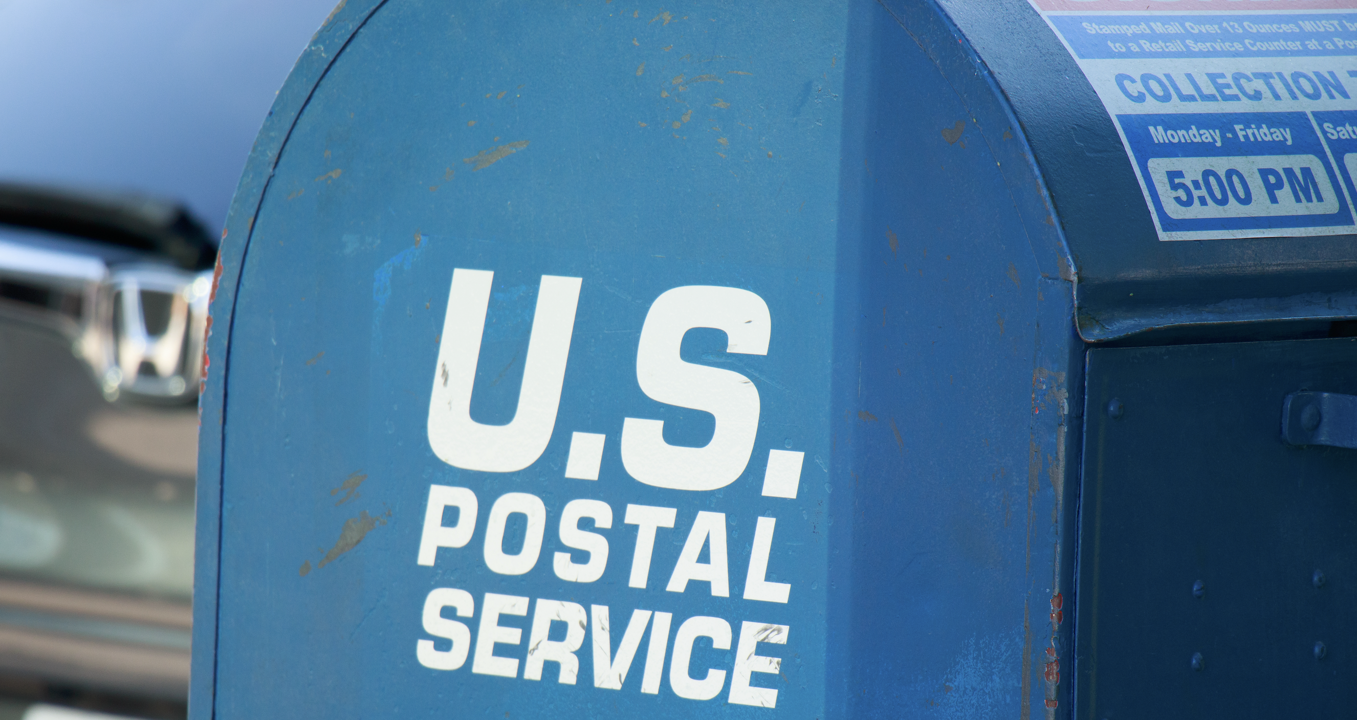 Blue U.S. Postal Service mailbox with collection schedule sign and white text branding