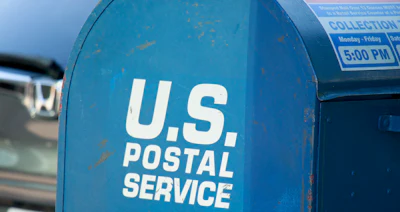 Blue U.S. Postal Service mailbox with collection schedule sign and white text branding