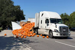 White semi-truck with overturned trailer spilling orange pumpkins across parking lot