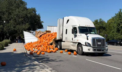 White semi-truck with overturned trailer spilling orange pumpkins across parking lot