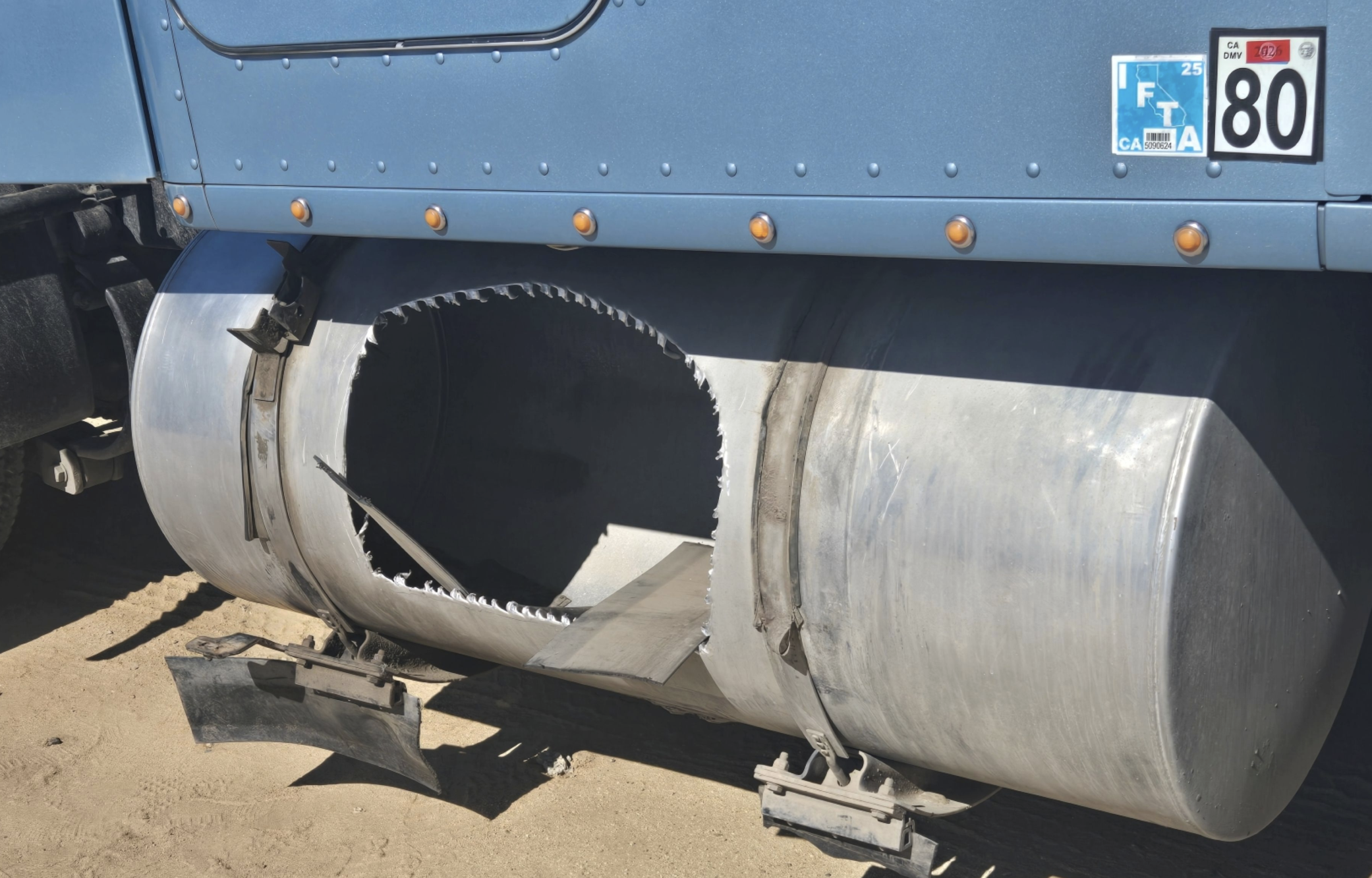 Damaged industrial pipe with jagged opening mounted on blue truck bed with road markers visible