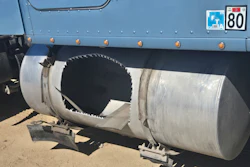 Damaged industrial pipe with jagged opening mounted on blue truck bed with road markers visible