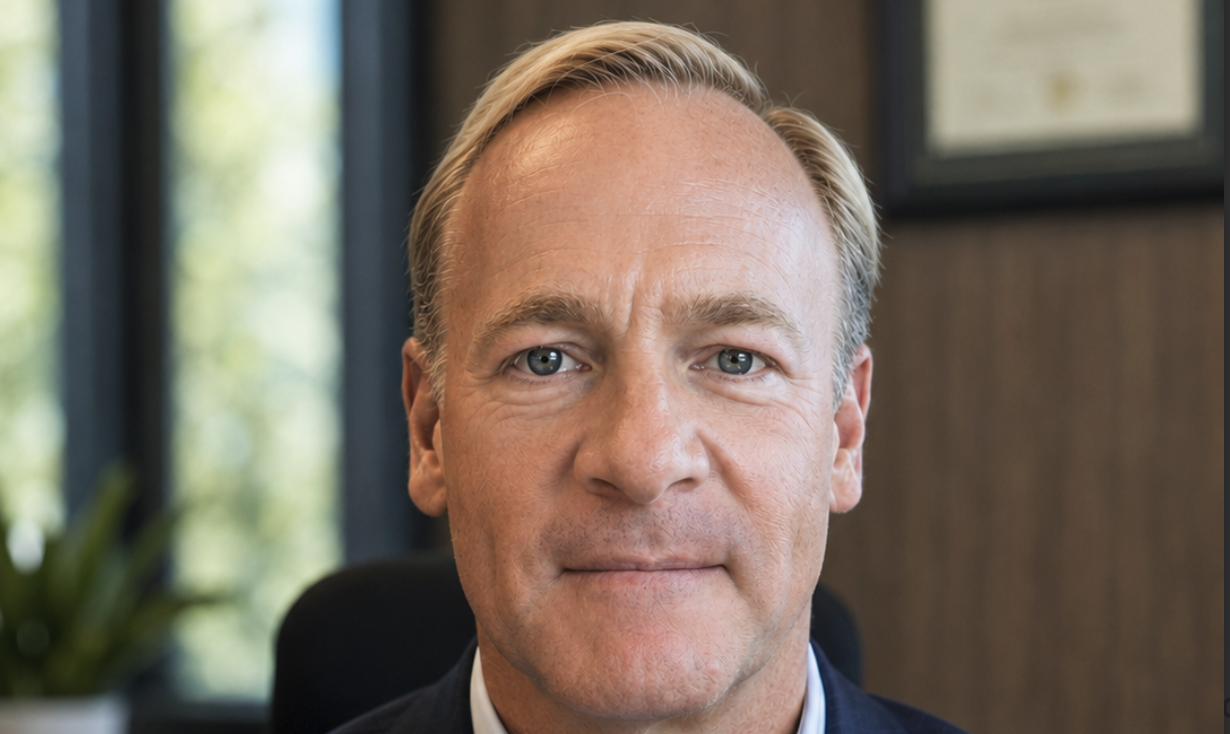 Professional headshot of a middle-aged man in dark navy suit against neutral office background