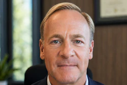 Professional headshot of a middle-aged man in dark navy suit against neutral office background
