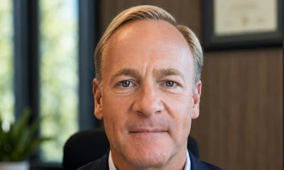 Professional headshot of a middle-aged man in dark navy suit against neutral office background