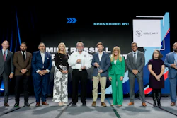 Group of business professionals standing on stage at formal event with Great West sponsorship banner