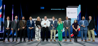 Group of business professionals standing on stage at formal event with Great West sponsorship banner