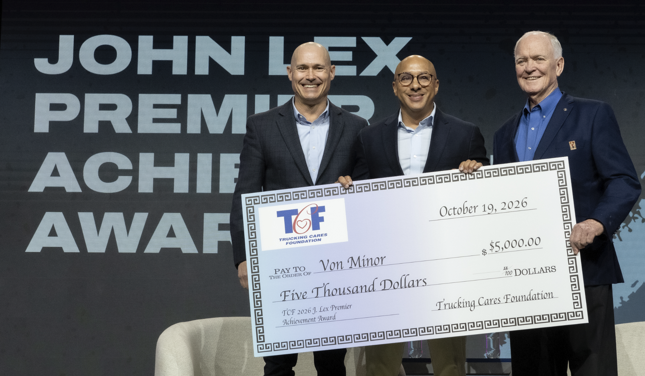 Three men in business attire holding a $5,000 ceremonial check from TCF at a Premier Achievement Award event.